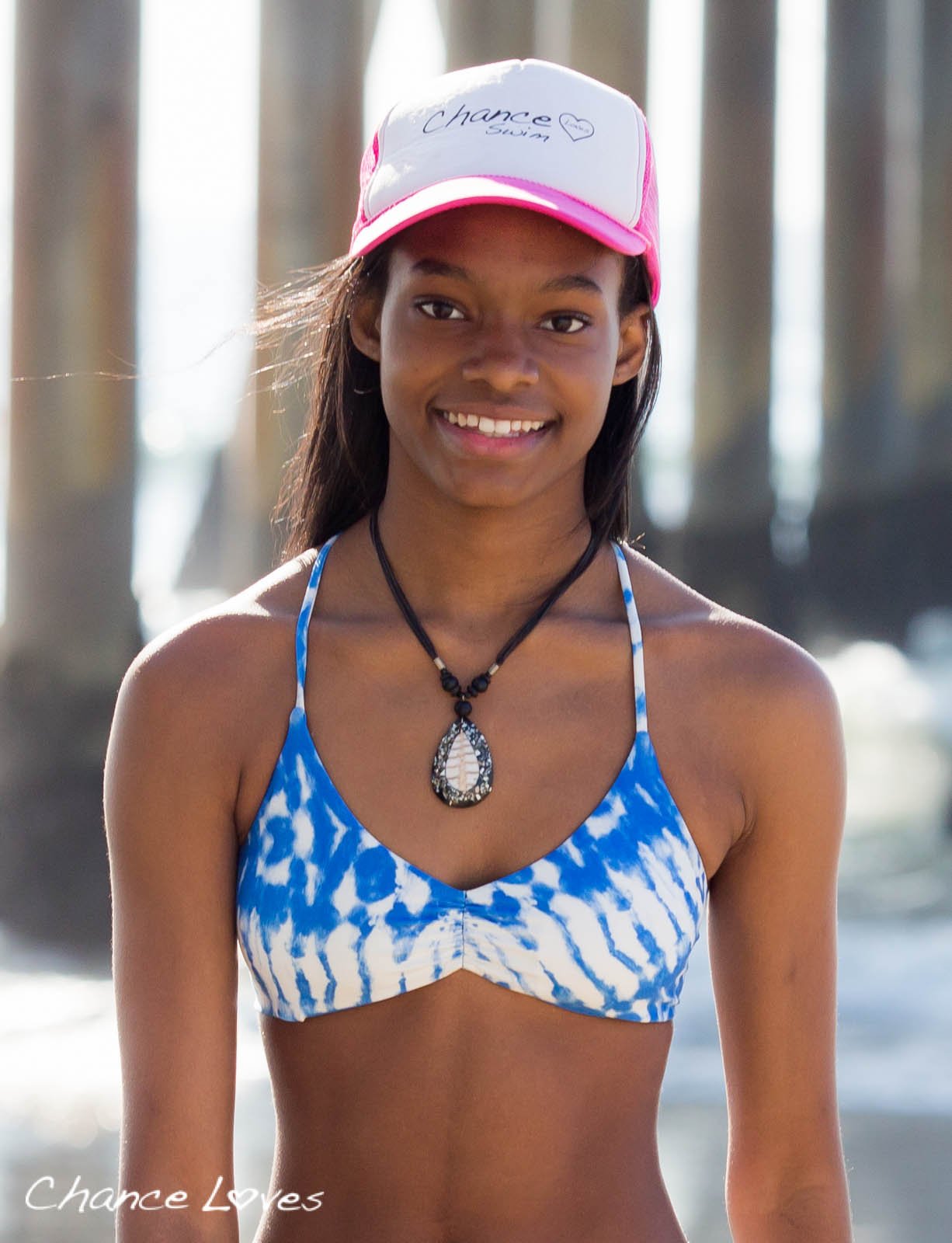 A smiling African American teen girl wearing a blue white tie dye bikini with removable padding on the beach in Venice
