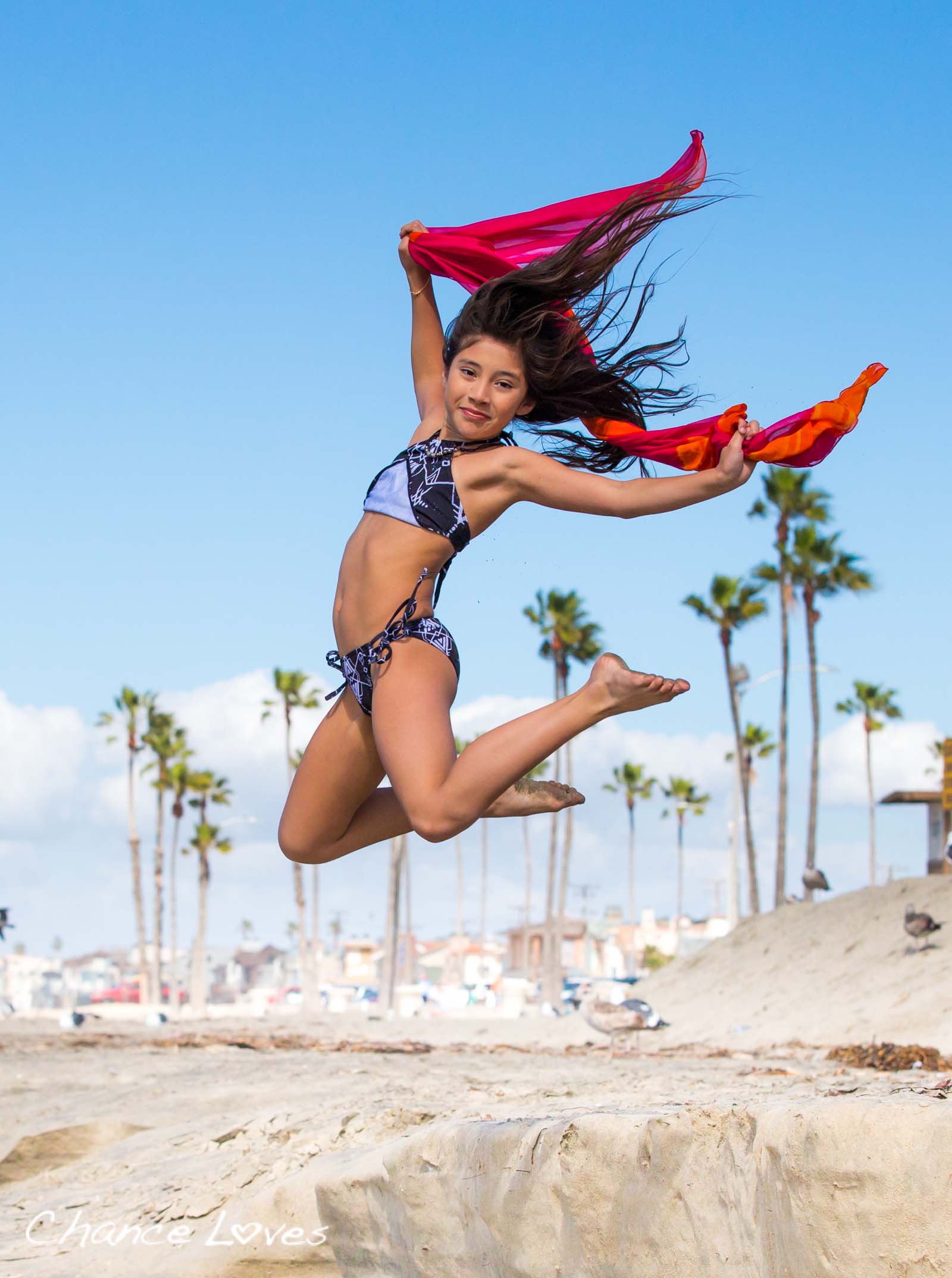 Athletic 10 year old girl is jumping off of a sand berm in her black and white swimsuit