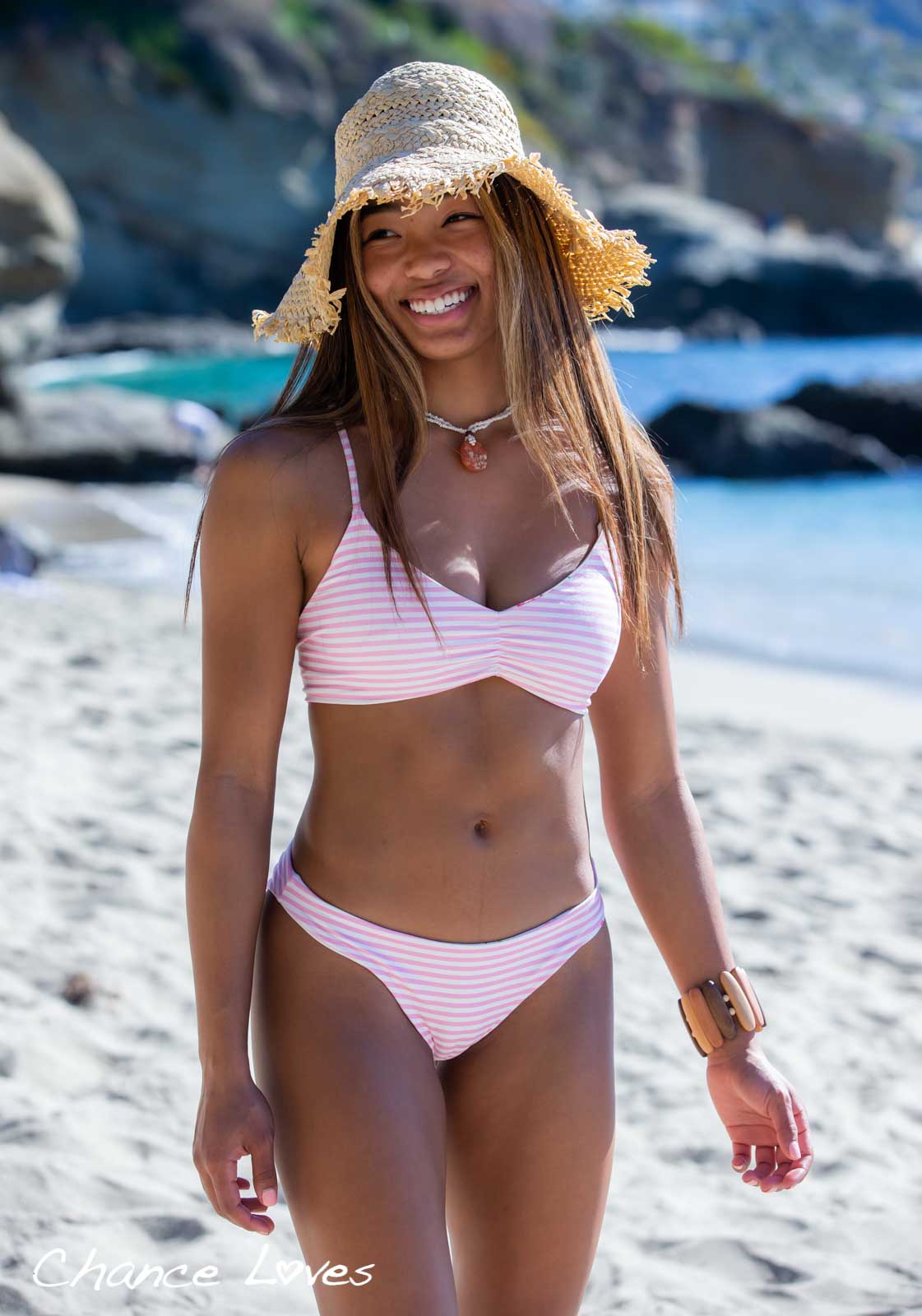 A smiling young woman on the beach wearing a sun hat and an adorable pink white stripe reversible floral bikini