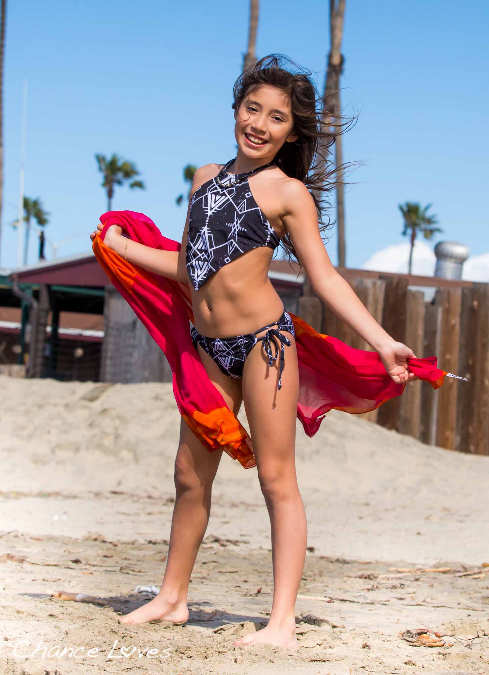 A 10 year old girl is laughing on the beach wearing a unique 2 piece swimsuit