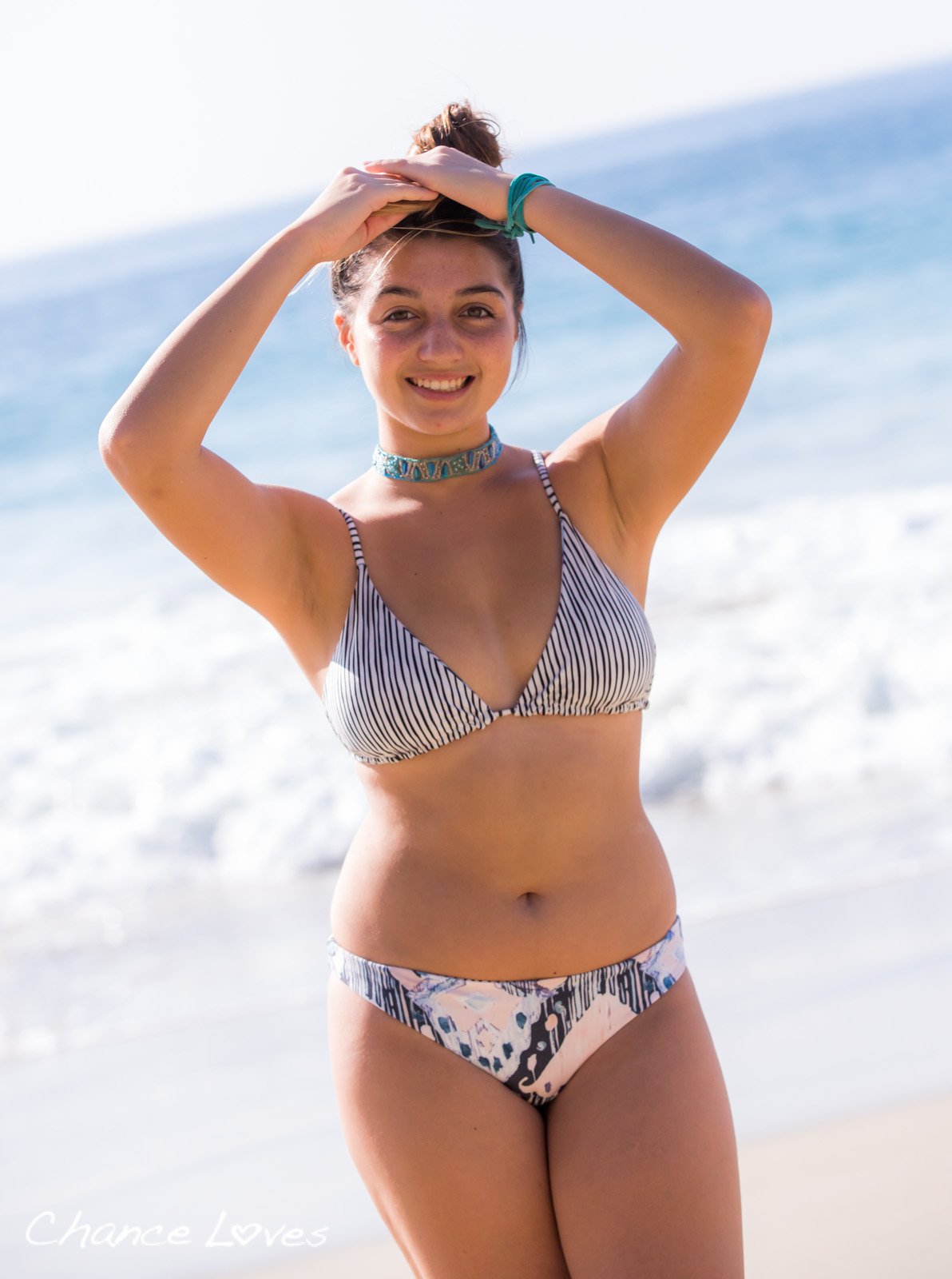 Young Woman on the beach, laughing and adjusting her pony tail at the same time, looking amazing in her reversible bikini.