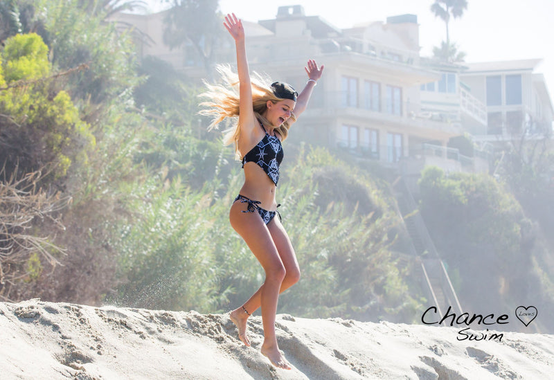 Running down a sand berm in Laguna Beach a beautiful girl wearing one Chance Loves' black swimsuits